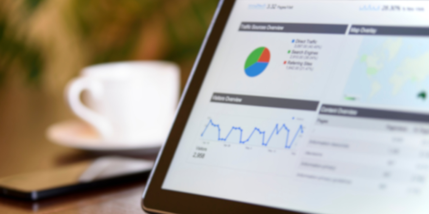 Tablet displaying performance analytics dashboard with graphs and charts, placed on a desk next to a smartphone and a coffee cup.