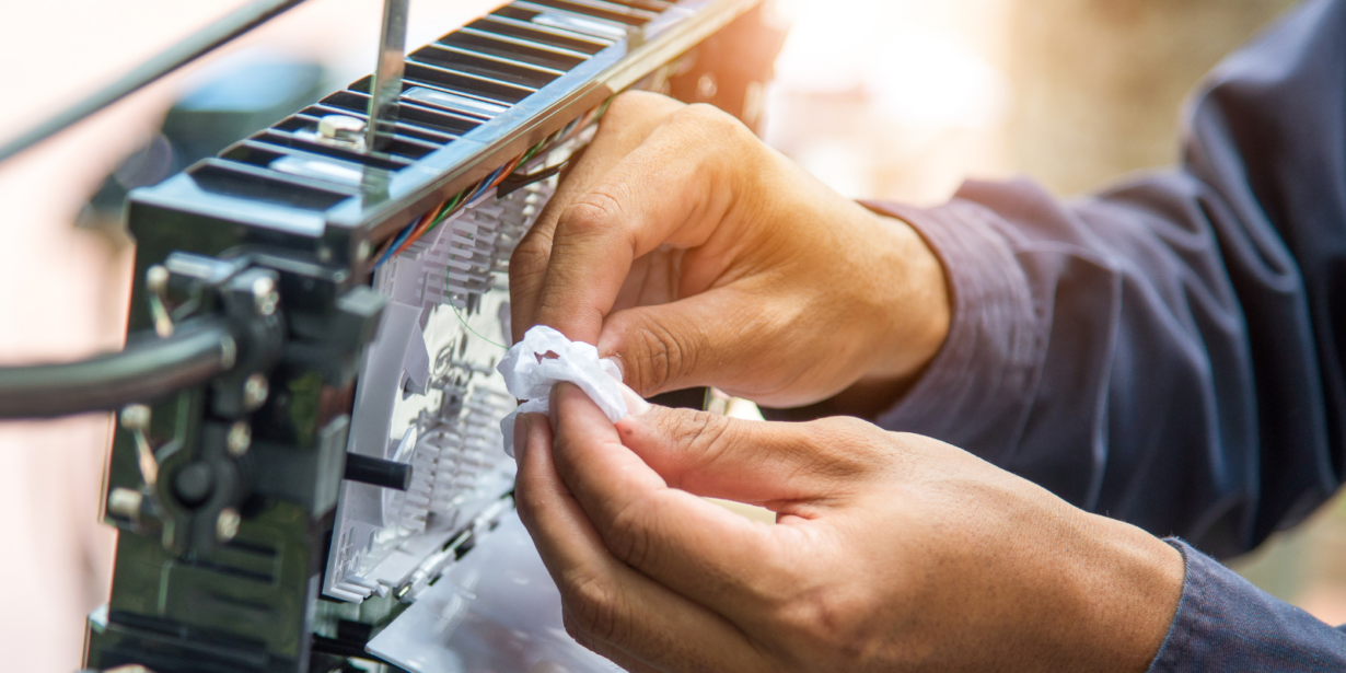A telecom subcontractor carefully works on a fiber optic connection, cleaning and securing a cable inside a distribution box.