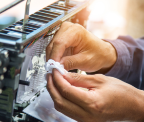 A telecom subcontractor carefully works on a fiber optic connection, cleaning and securing a cable inside a distribution box.
