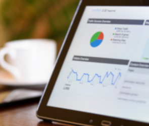 Tablet displaying performance analytics dashboard with graphs and charts, placed on a desk next to a smartphone and a coffee cup.
