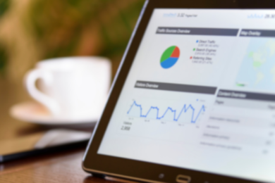 Tablet displaying performance analytics dashboard with graphs and charts, placed on a desk next to a smartphone and a coffee cup.